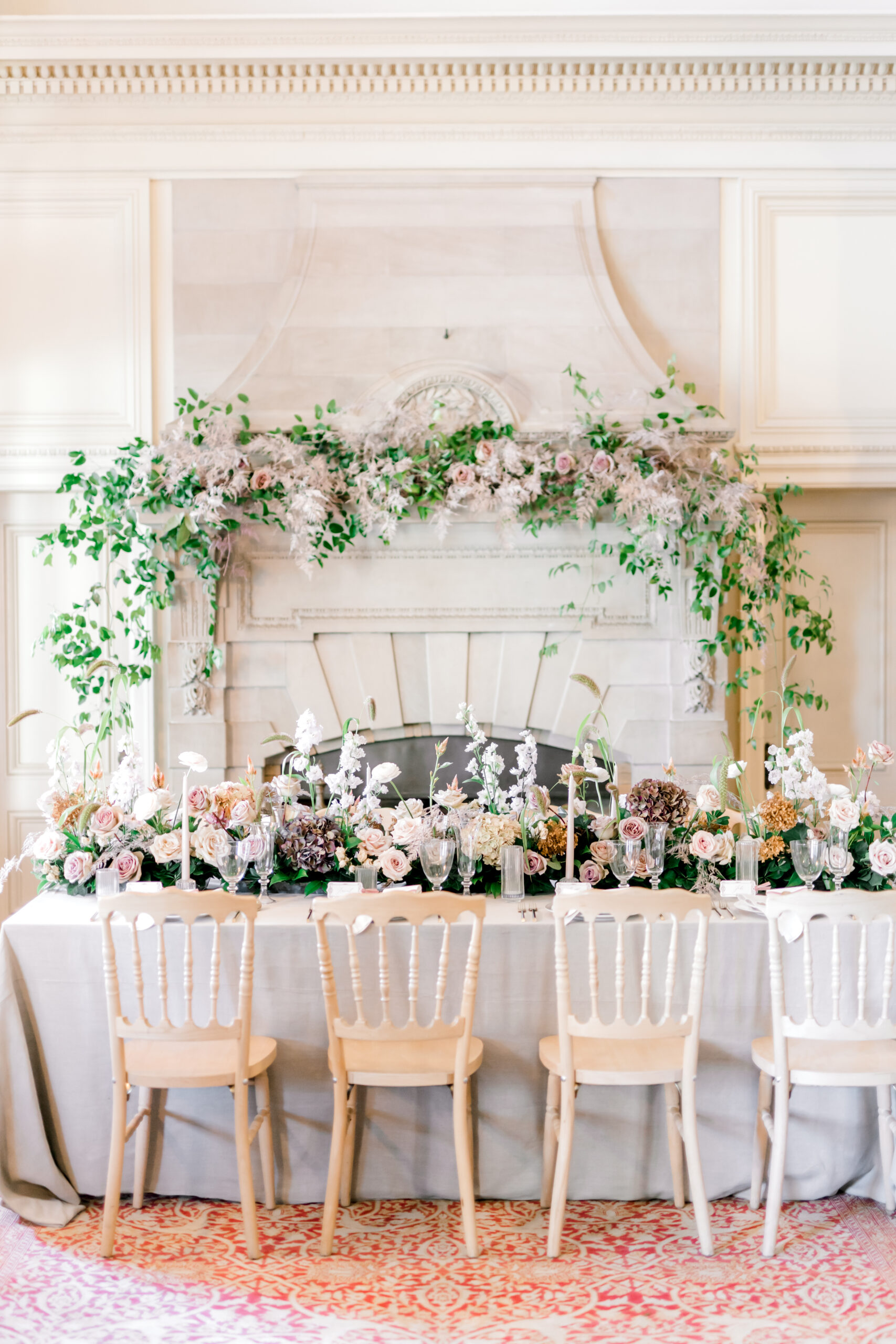 Large floral installation over a fireplace with a tablescape in front, ready for a wedding