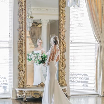Bride looking at herself in a large ornate mirror
