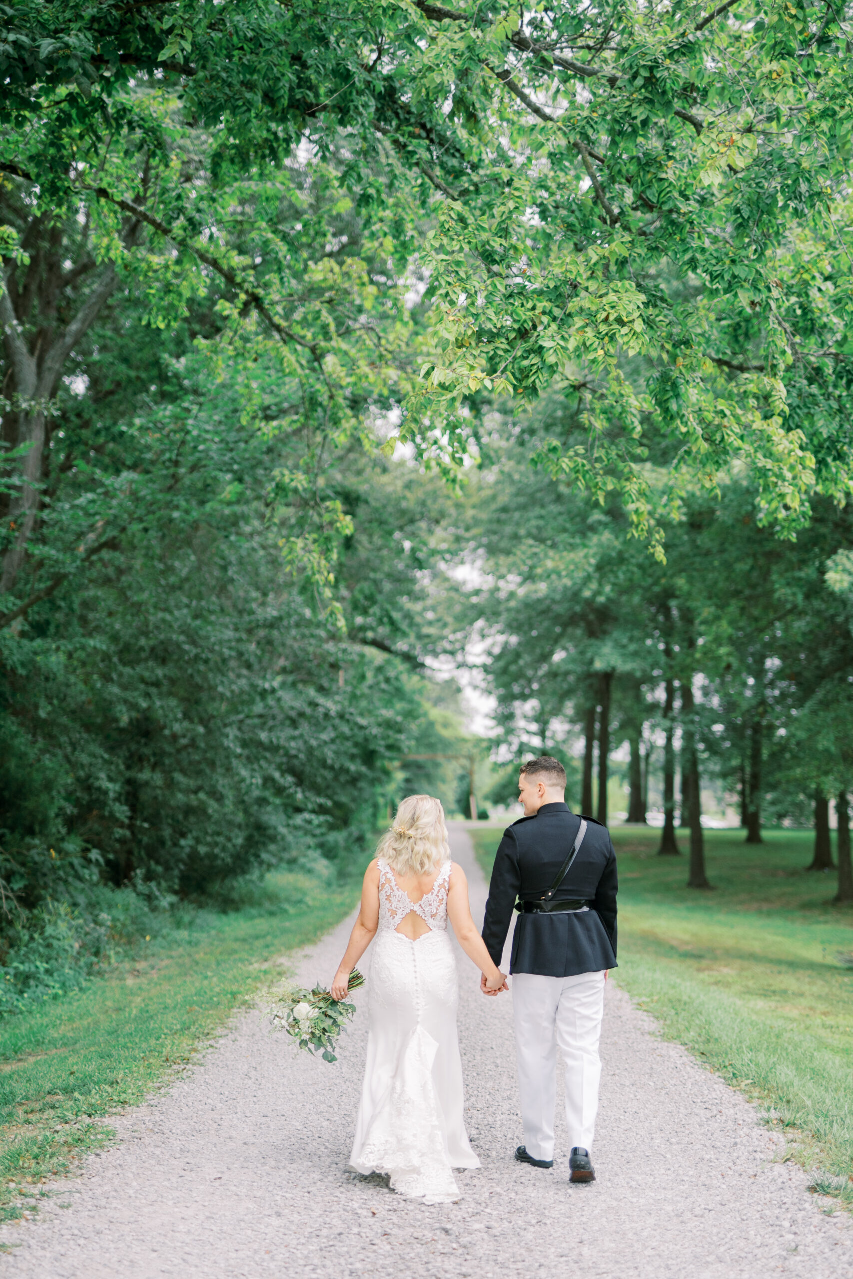 Bride and groom walking along a shaded road under trees at their wedding