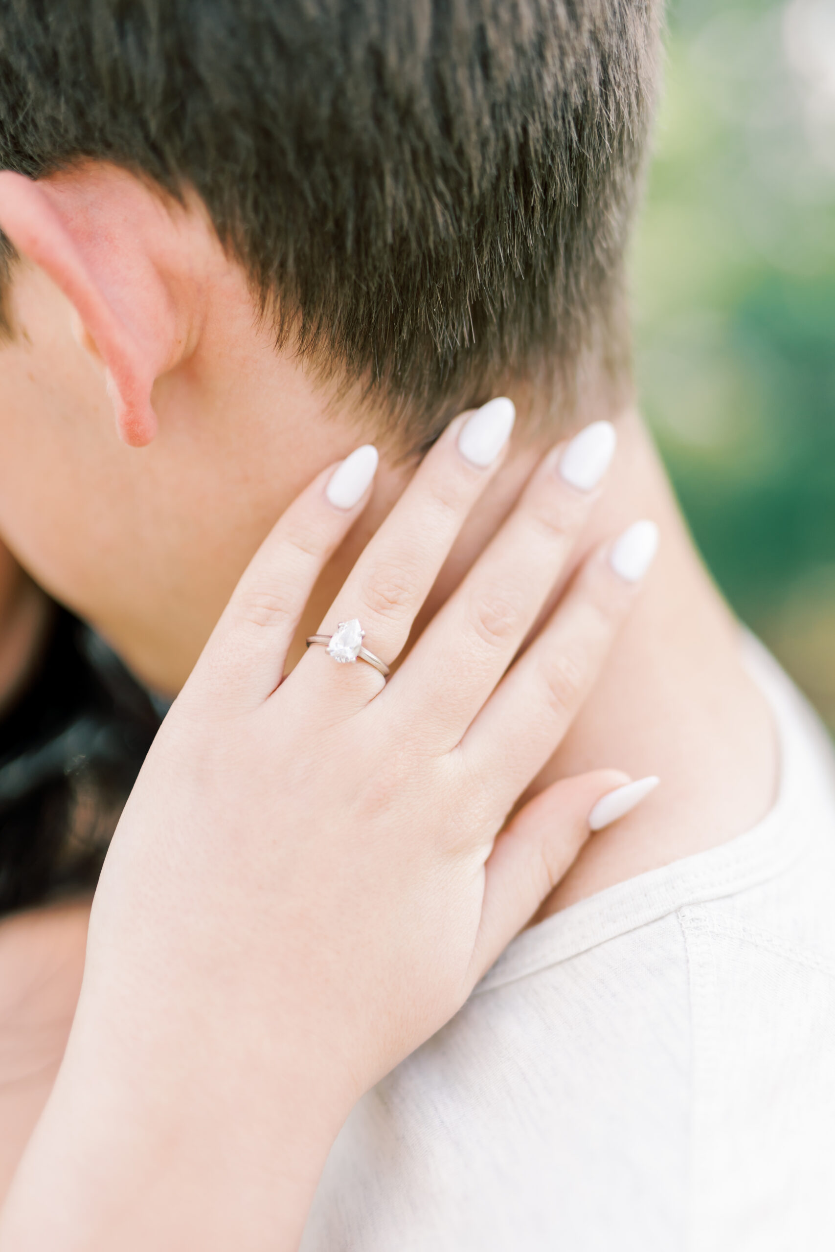 back of mans head with womans hand around neck, engagement ring featured prominently